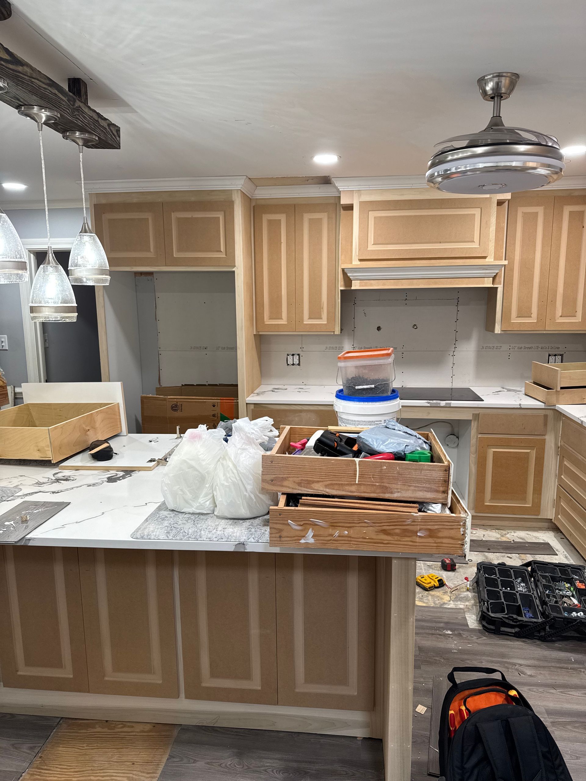 Cluttered kitchen under renovation with unfinished cabinets, island, and tools on counters and floor