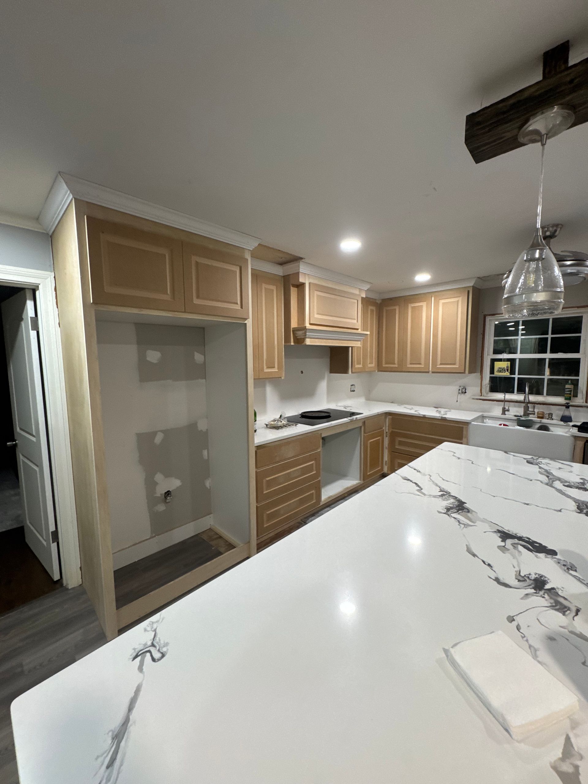 Modern kitchen with light wood cabinets, white marble countertop, stainless range, and hanging glass pendant light