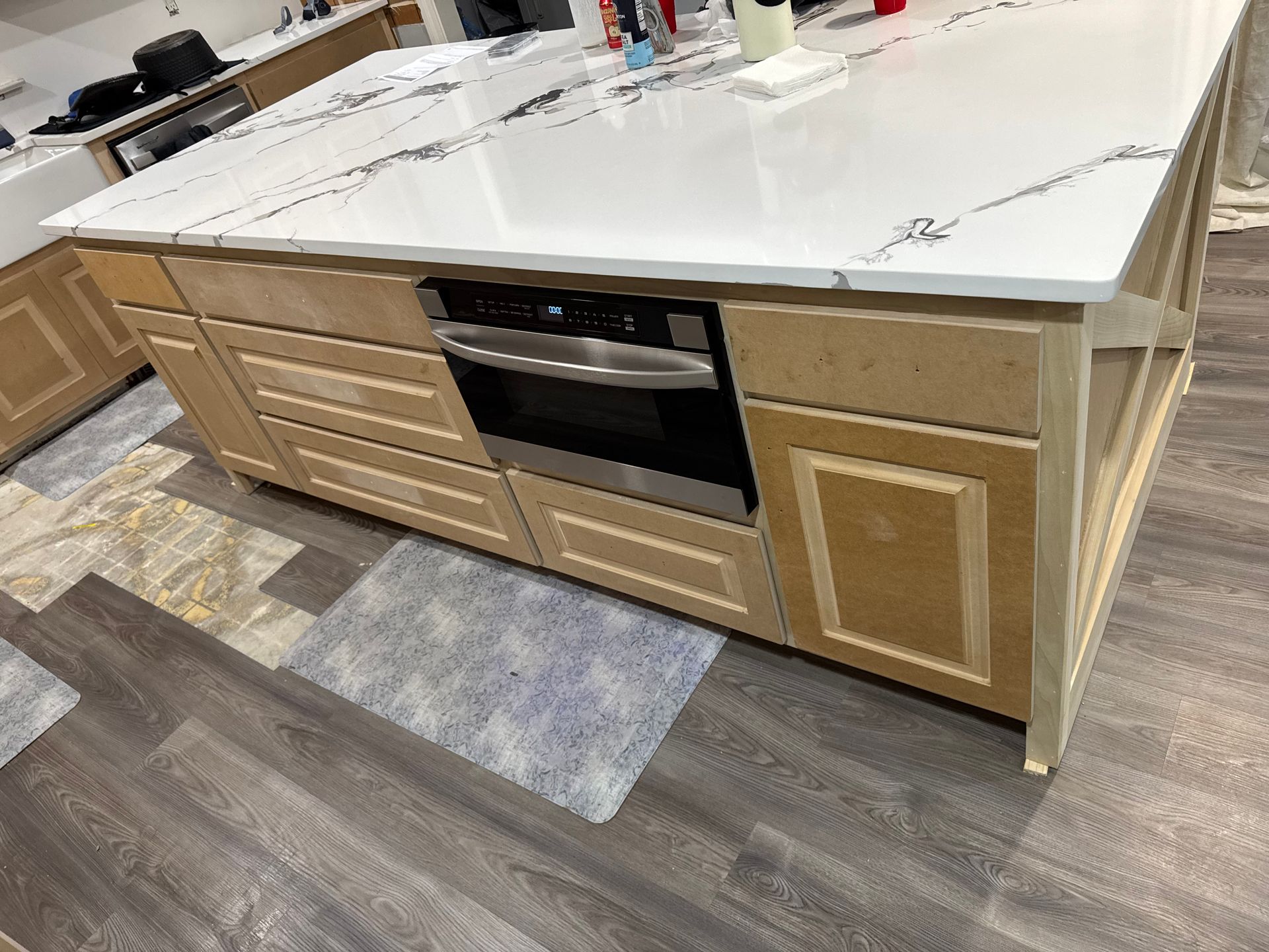 Kitchen island with white countertop and light wood cabinets under renovation, tools visible on the counter.