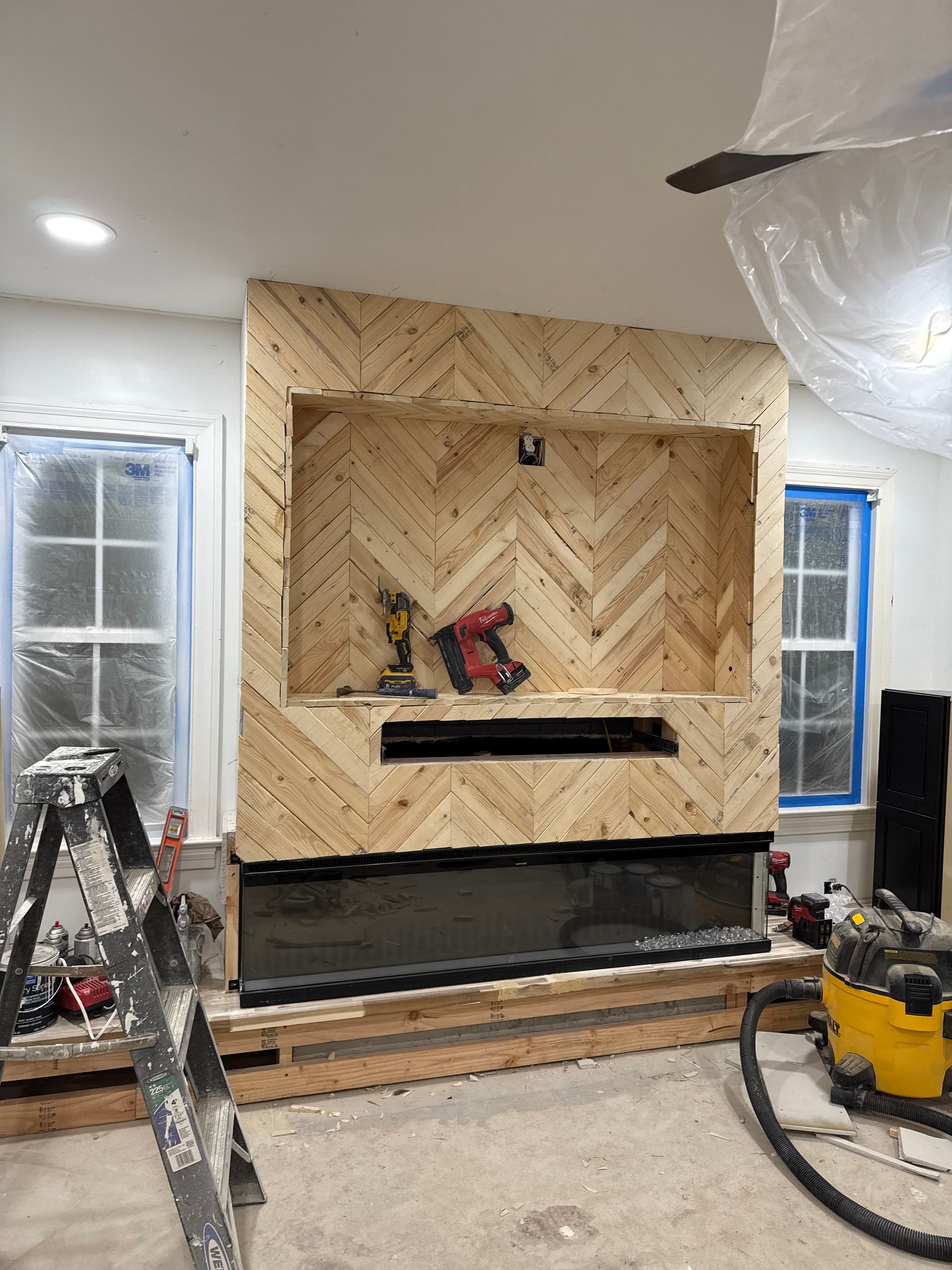 Living room with a herringbone wood fireplace surround under construction, tools and ladder in front