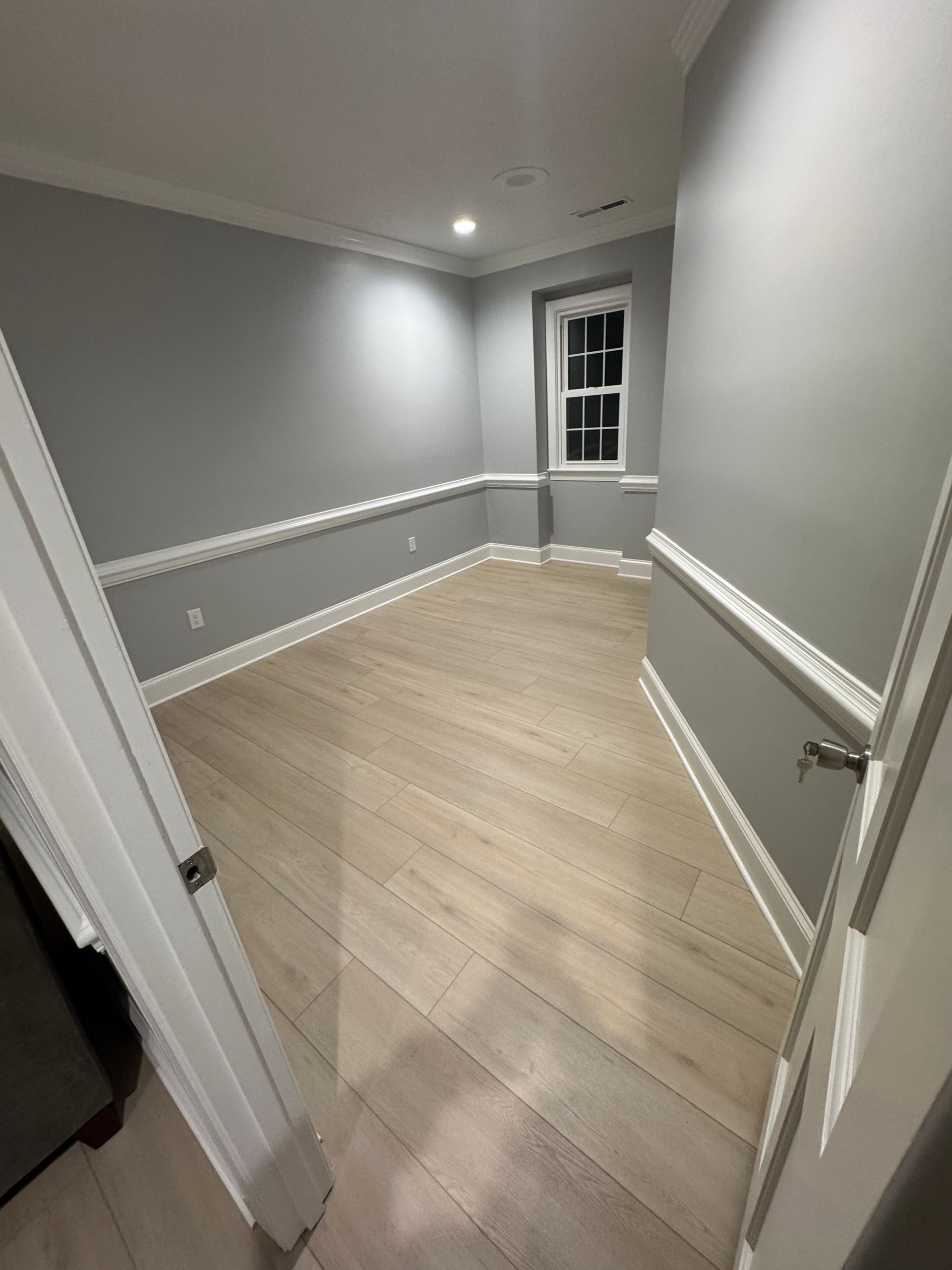 Empty gray room with light wood floors, white trim, and a small window.