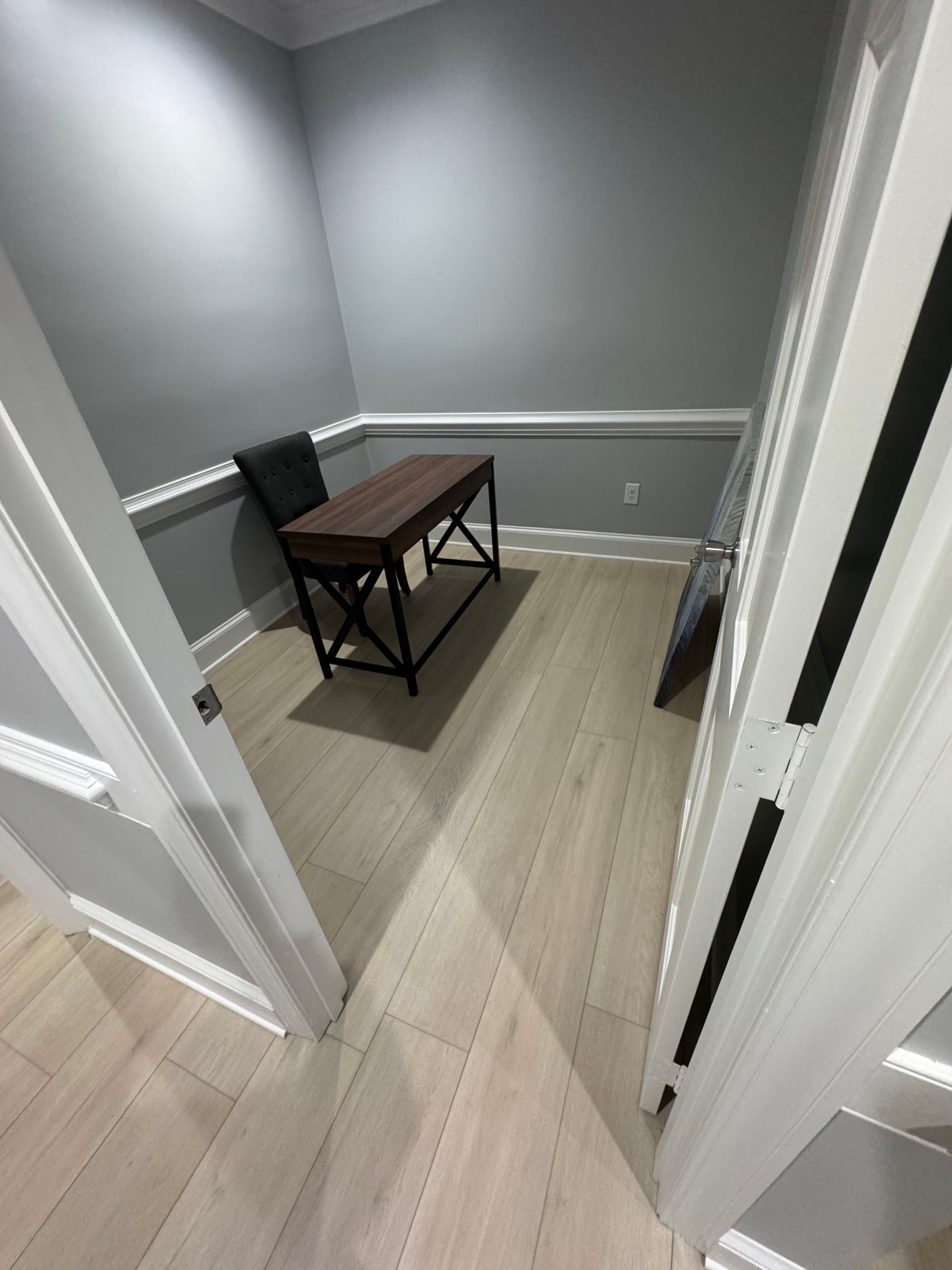 Small gray hallway with a wooden bench and white doorways leading into a narrow room.