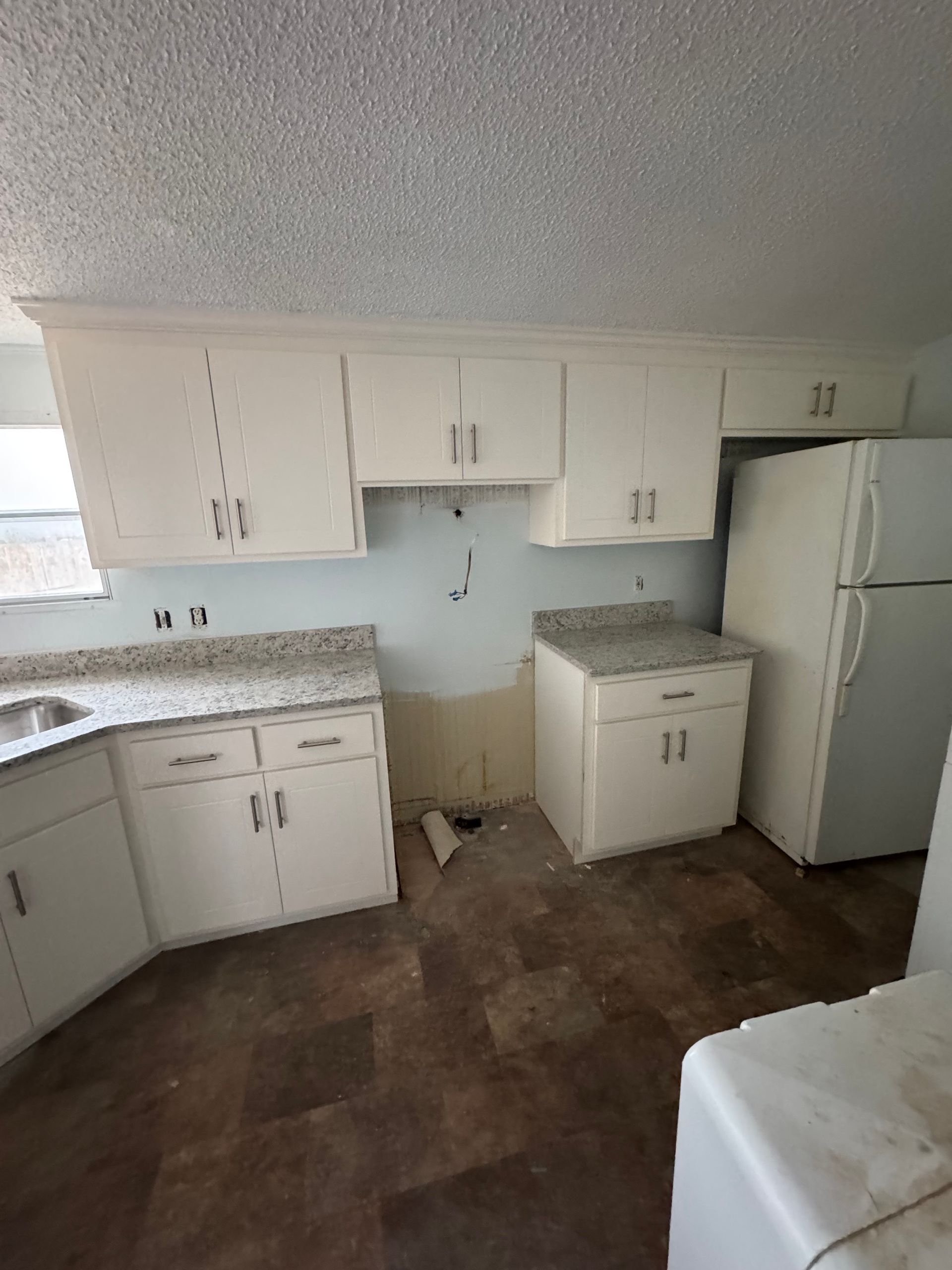 Small white kitchen with cabinets, stove nook, sink, countertop, and a refrigerator on the right.