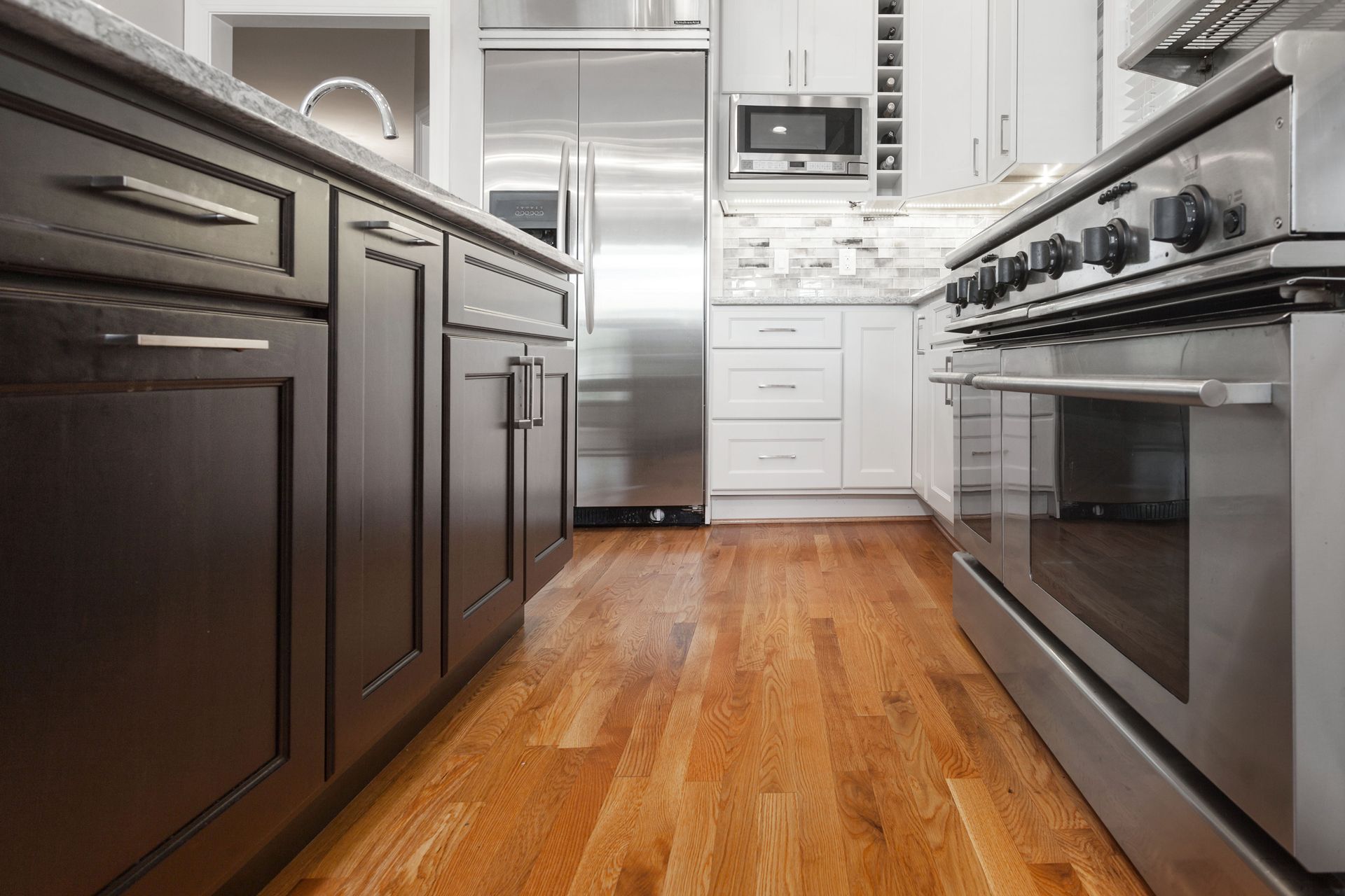 Kitchen with wood floors, dark cabinets, stainless steel appliances, and white cabinets.