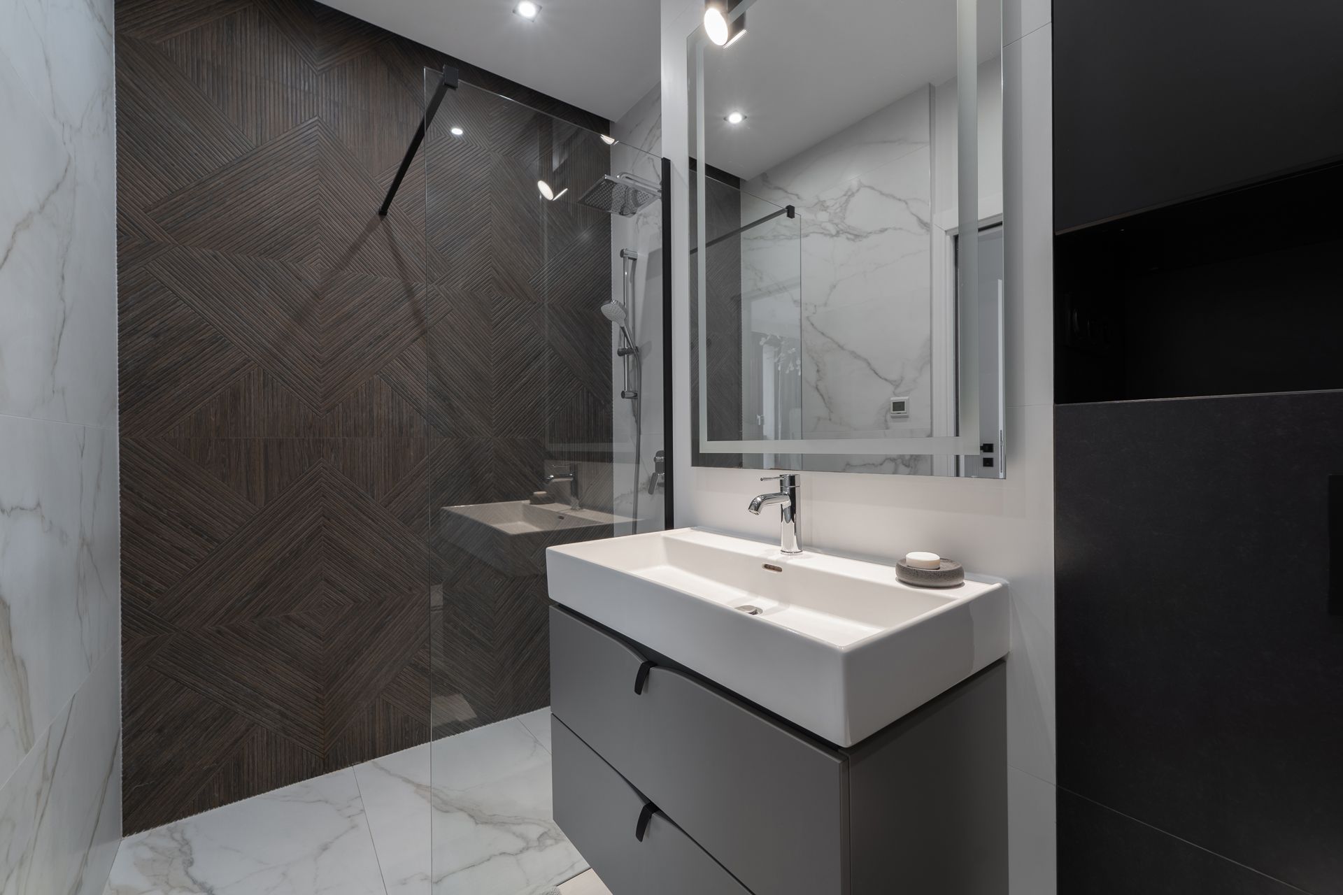 Modern bathroom with gray vanity, white sink, patterned wall, shower, and mirror.