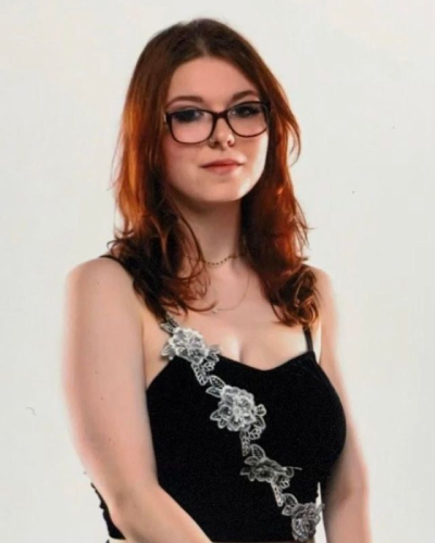A woman with red hair wearing glasses and a black top