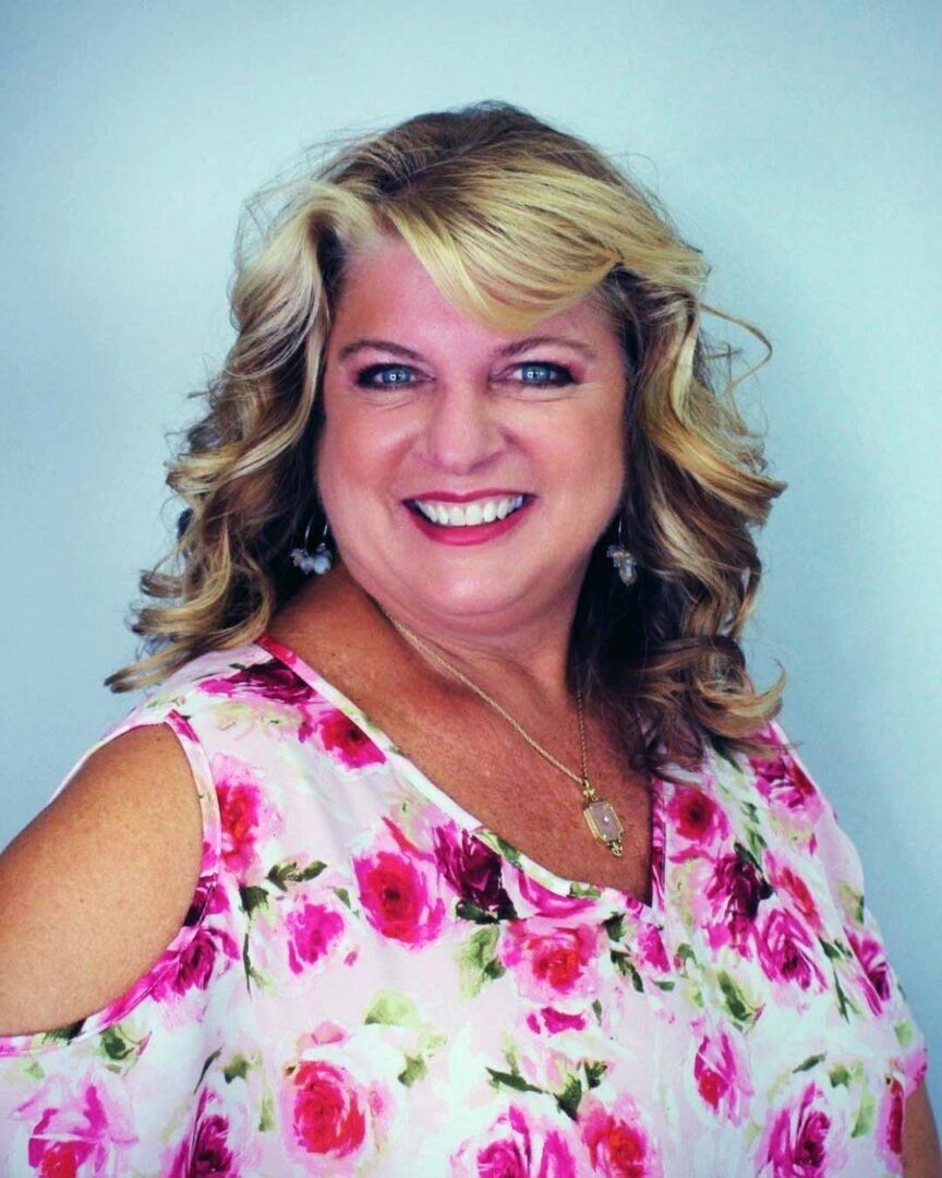 a woman in a pink floral shirt is smiling for the camera .