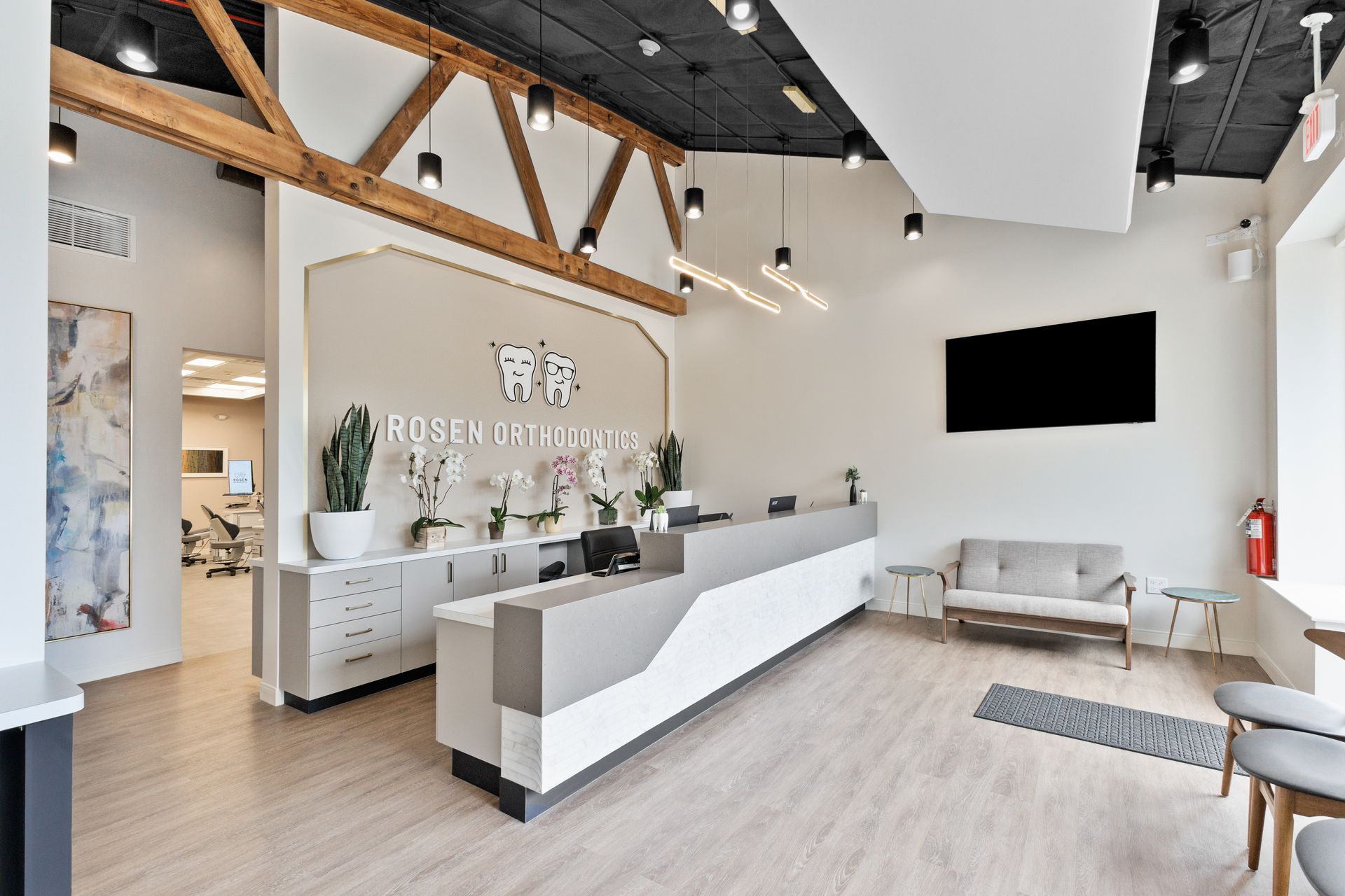 Modern clinic reception with white desk, light wood floors, exposed beams, and waiting area seating