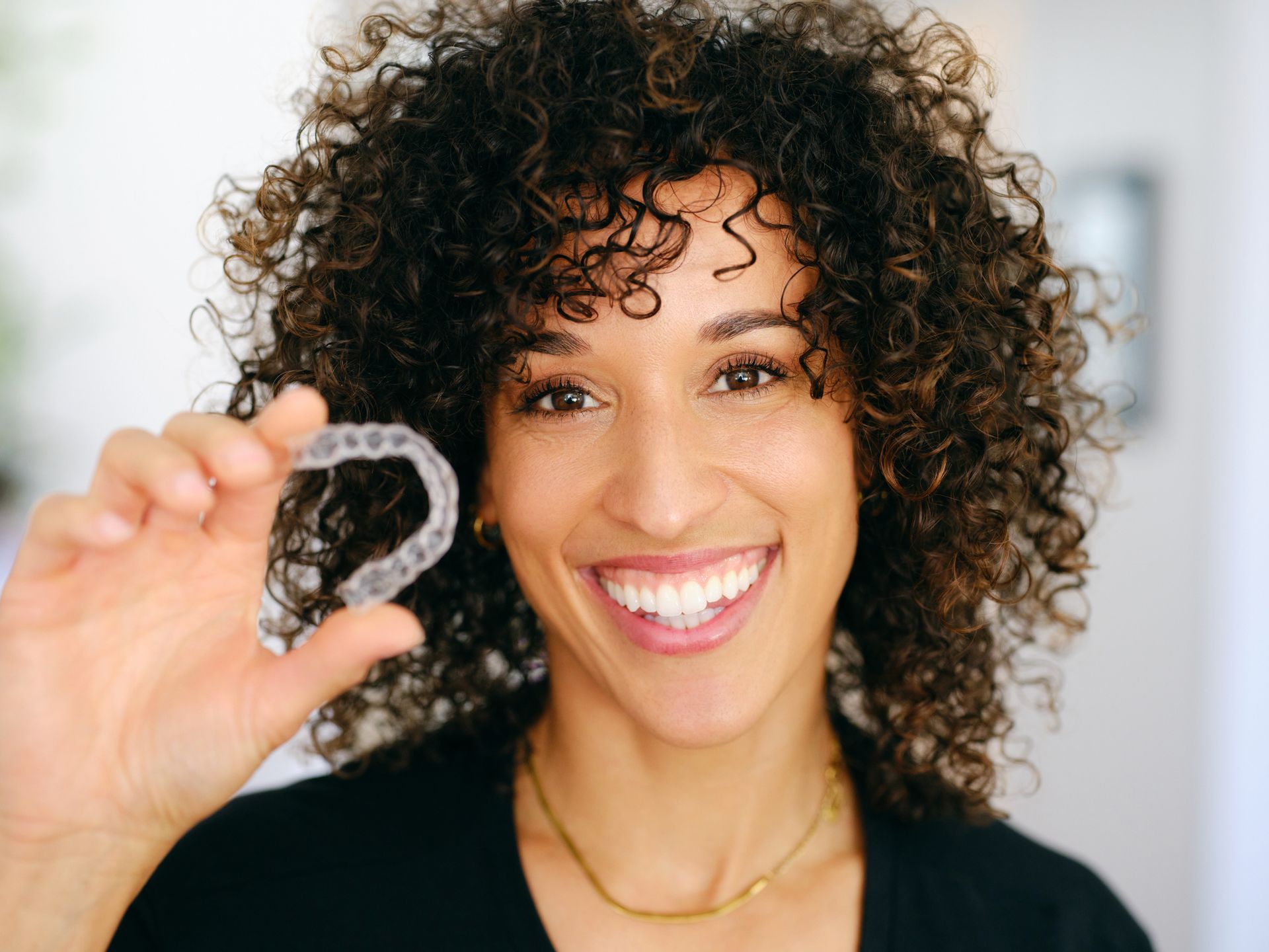 Smiling woman holding a toothbrush, promoting dental hygiene and Invisalign treatment.