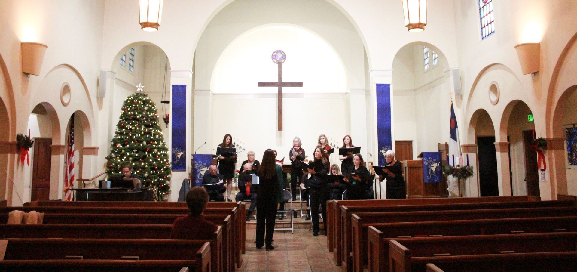 Choir performing in a church with Christmas tree and cross.