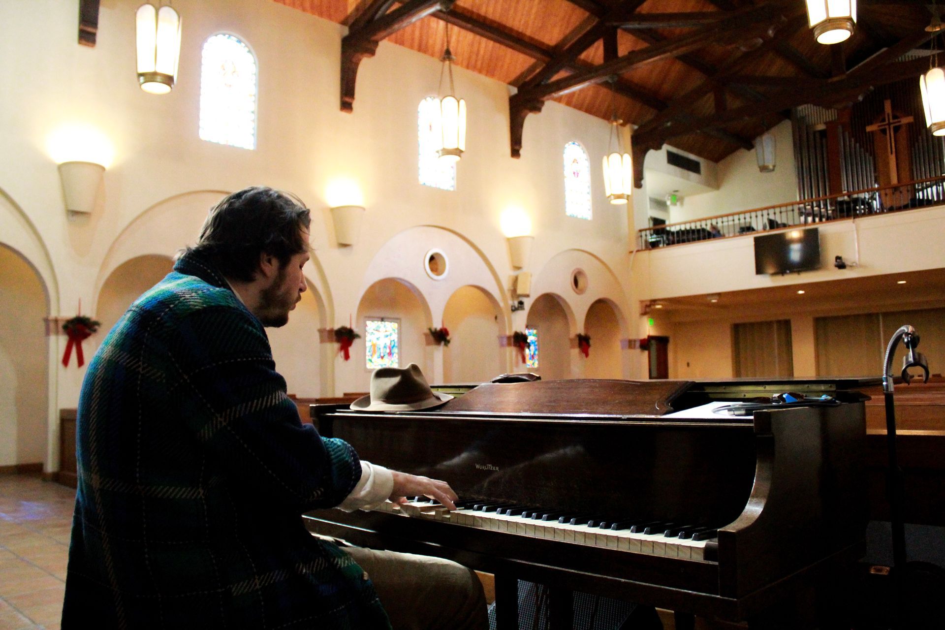Person playing piano in a church. Wooden beams, arched windows. Warm lighting.