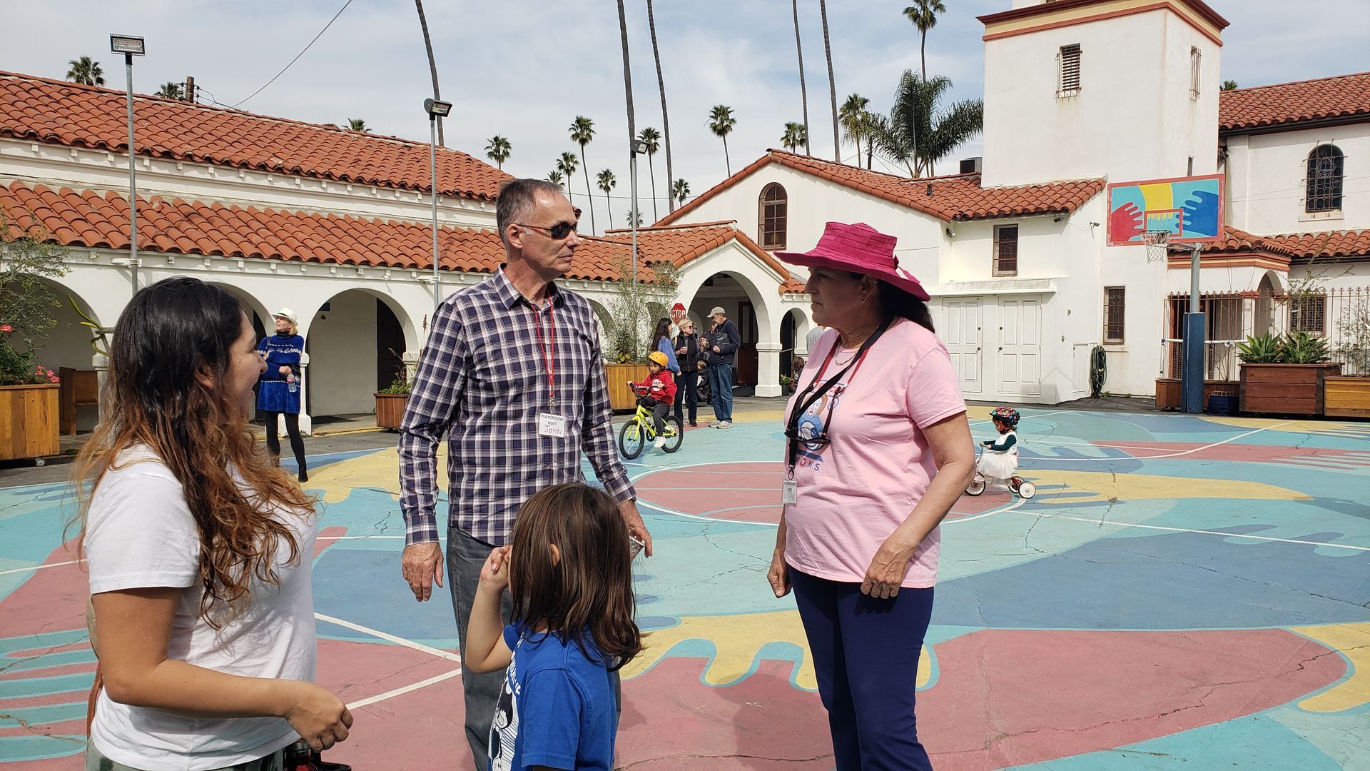 People talking in a courtyard with a building in the background. Colorful ground.