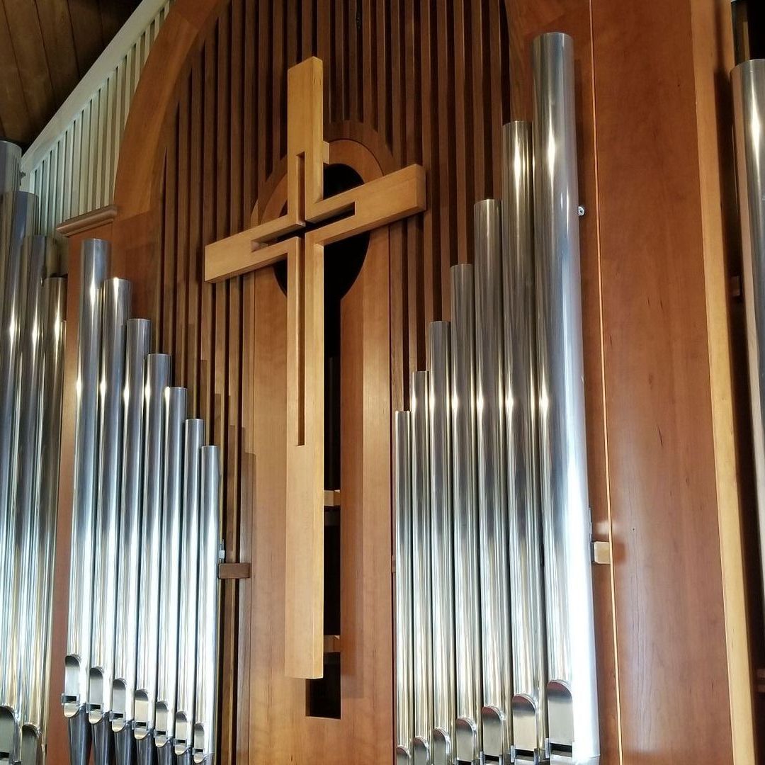 Church organ with silver pipes and a wooden cross.