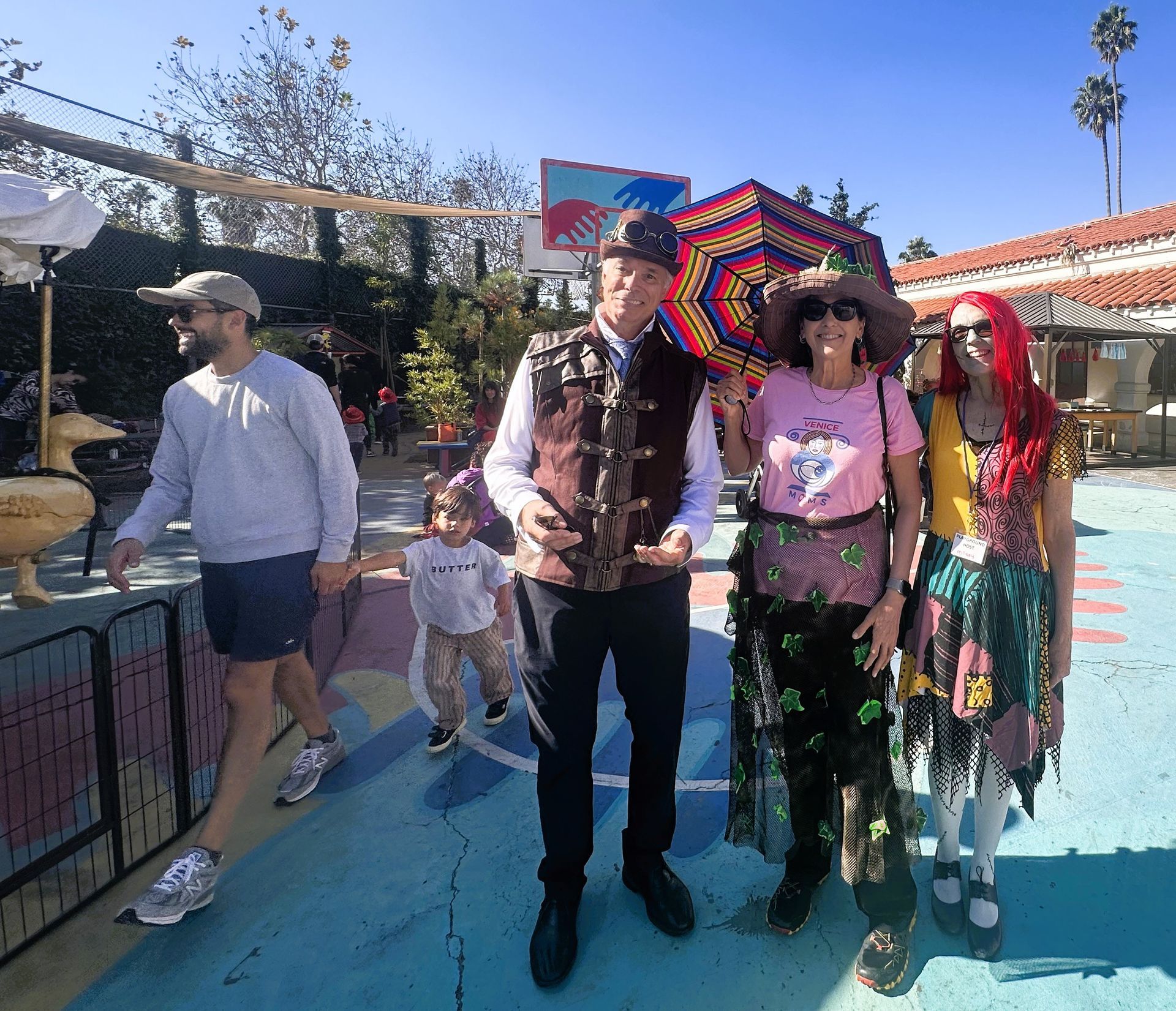 People in costume posing outdoors, one with umbrella. Others nearby, sunny day.