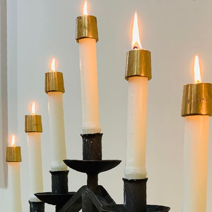 Candle holder with six lit white candles, each topped with a gold holder, against a white background.