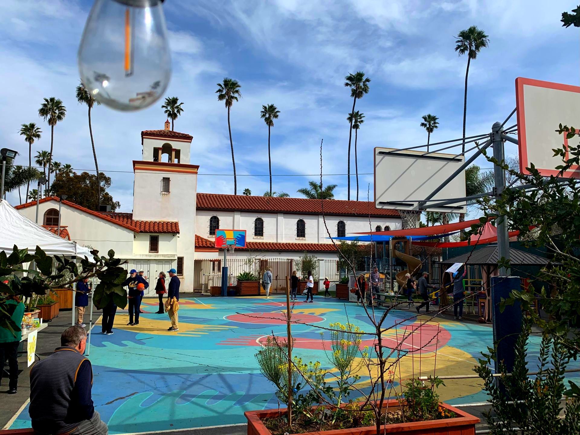 Basketball court with colorful pavement, palm trees, and a white building in the background.