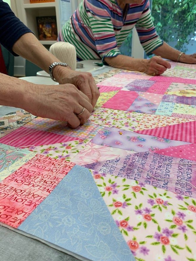Hands piecing colorful fabric squares to create a quilt.