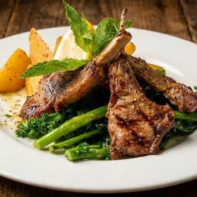 Grilled lamb chops with asparagus and potato wedges on a white plate, garnished with mint leaves