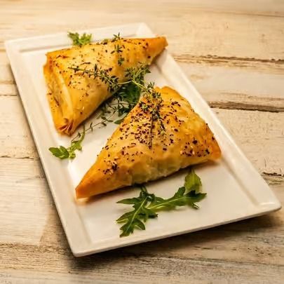 Two golden-brown baked pastries on a white plate, garnished with herbs on a wooden table.
