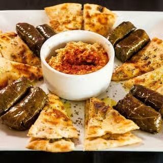 Plate of stuffed grape leaves and pita wedges arranged around a bowl of dip.