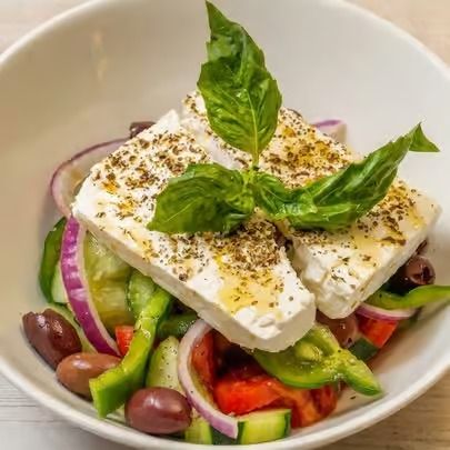 Greek salad with feta, tomatoes, cucumbers, olives, and basil in a white bowl