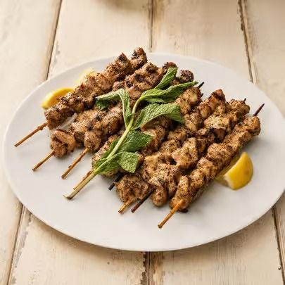 Grilled meat skewers on a white plate with mint garnish and lemon wedges