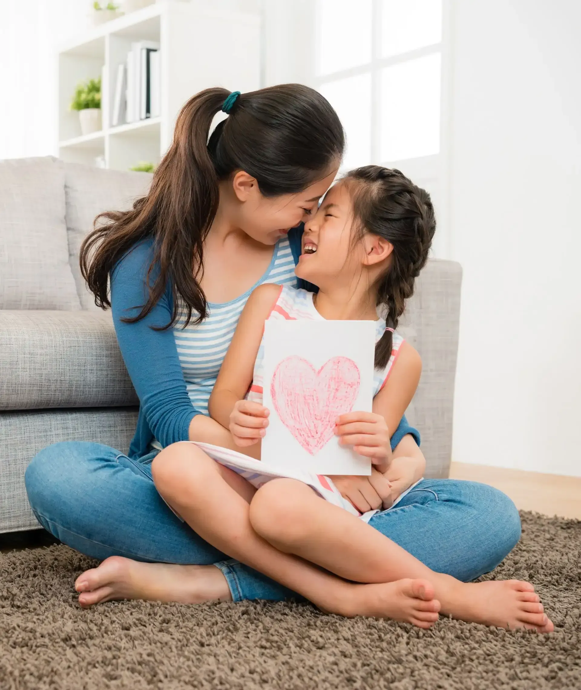 A mother and daughter are sitting on the floor holding a drawing of a heart.