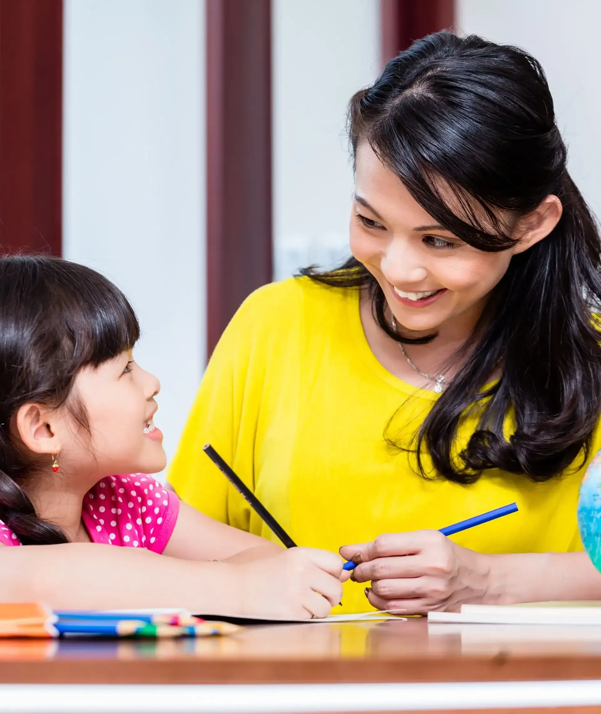 A woman is helping a little girl with her homework at a table.
