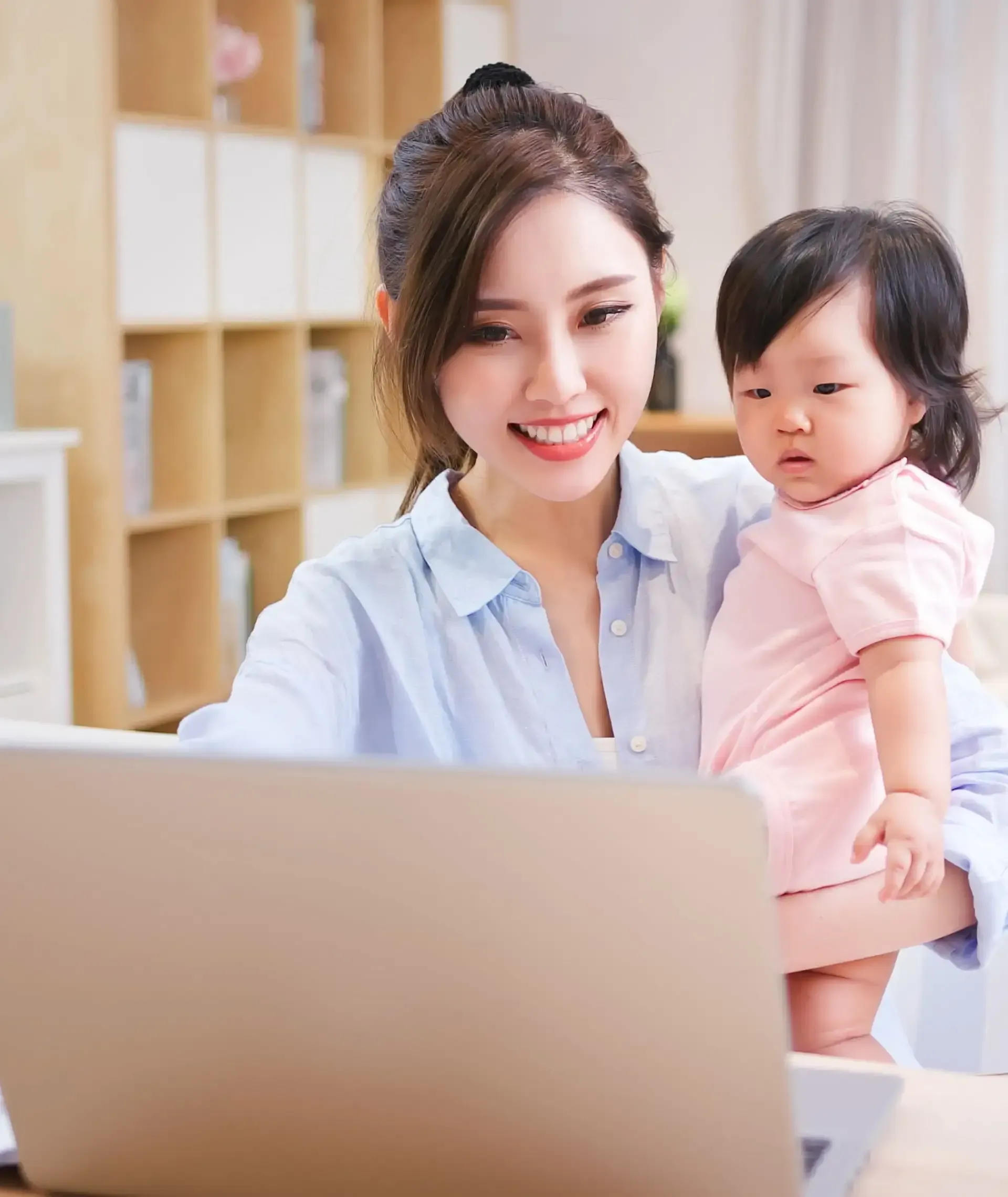 A woman is holding a baby while using a laptop computer.