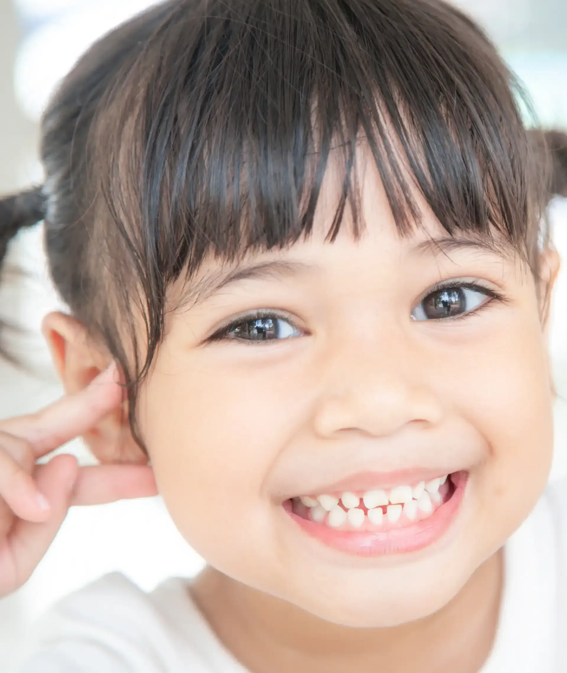 A little girl is smiling and touching her ear.