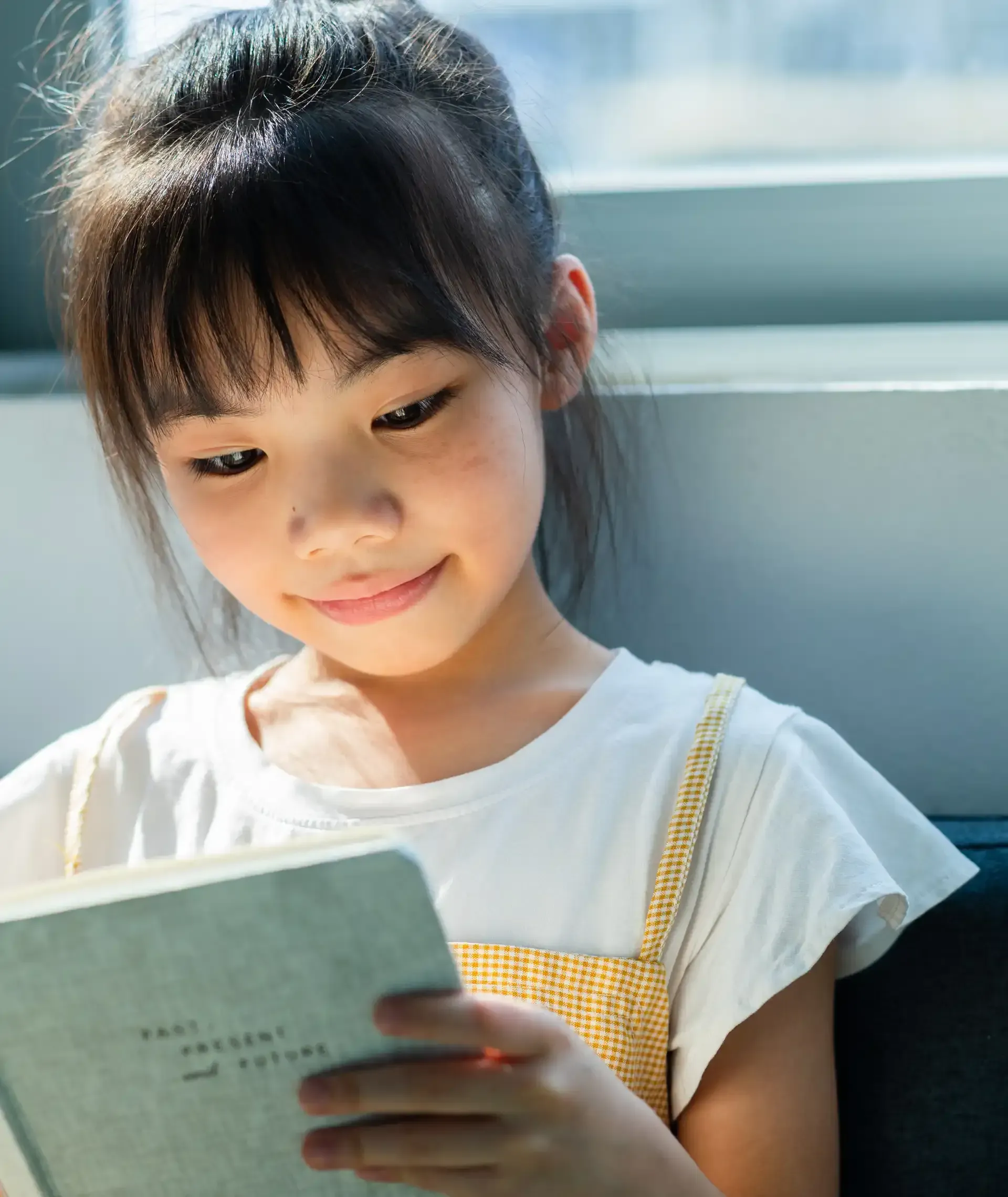 A little girl is reading a book and smiling.