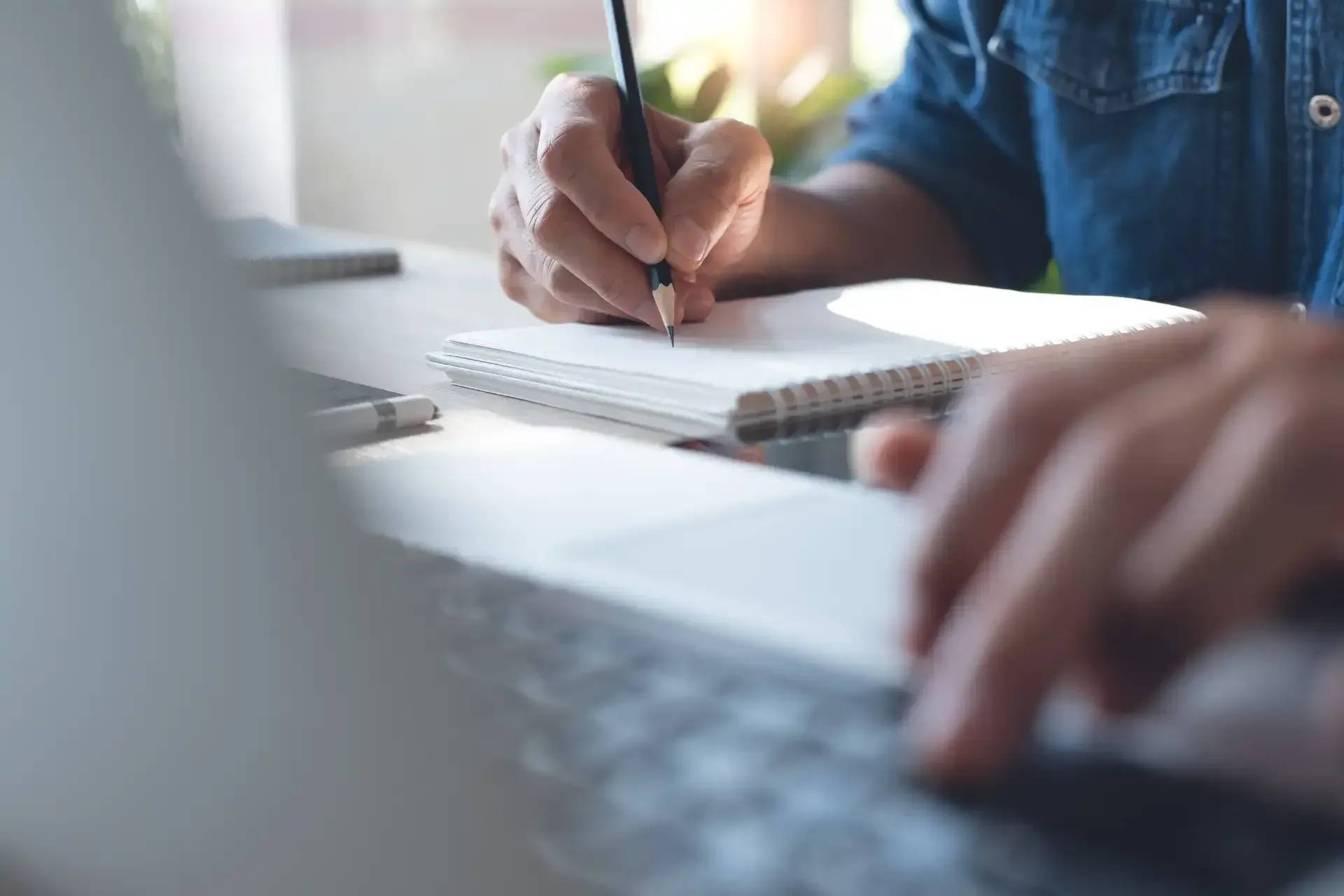 a person is writing in a notebook while using a laptop computer .