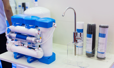 Countertop water filtration setup with blue-and-white filter unit, faucet, and several filter cartridges.