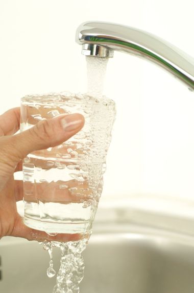 Hand pouring water into a clear glass held over a sink