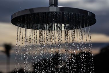 Rain falling from a round outdoor shower against a dusk sky