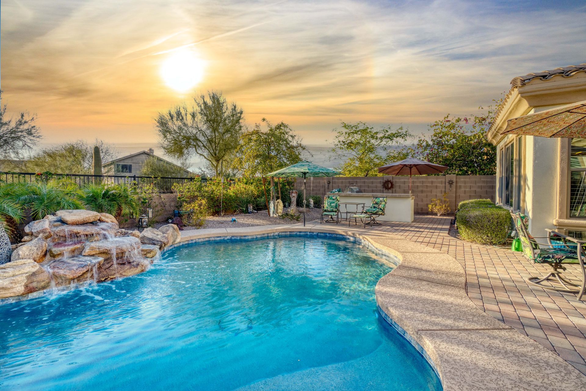 A large swimming pool with a waterfall in the backyard of a house.