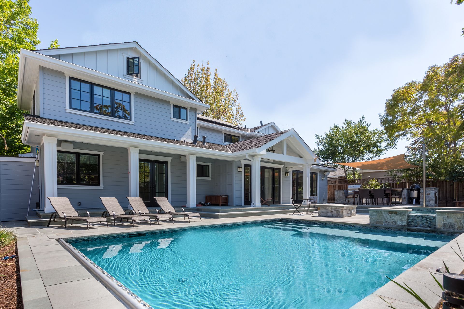 Swimming pool installed by Elite Outdoor Living Solutions in OKC, spa, and fire pit; home with white columns, sunny day.