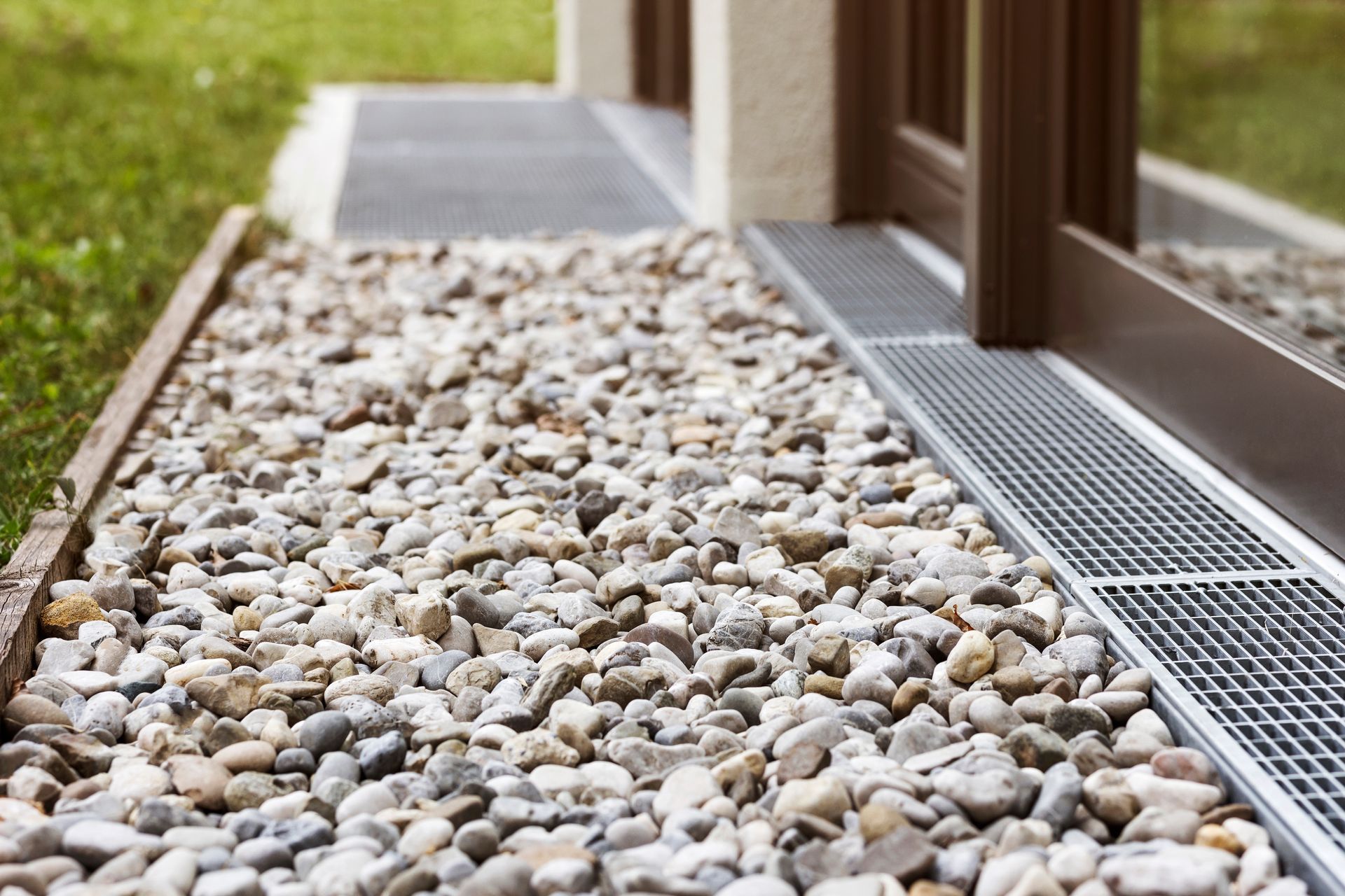 Elite Outdoor Living Solutions installed a decorative sidewalk drain filled with rocks and a metal grate in Norman, OK.