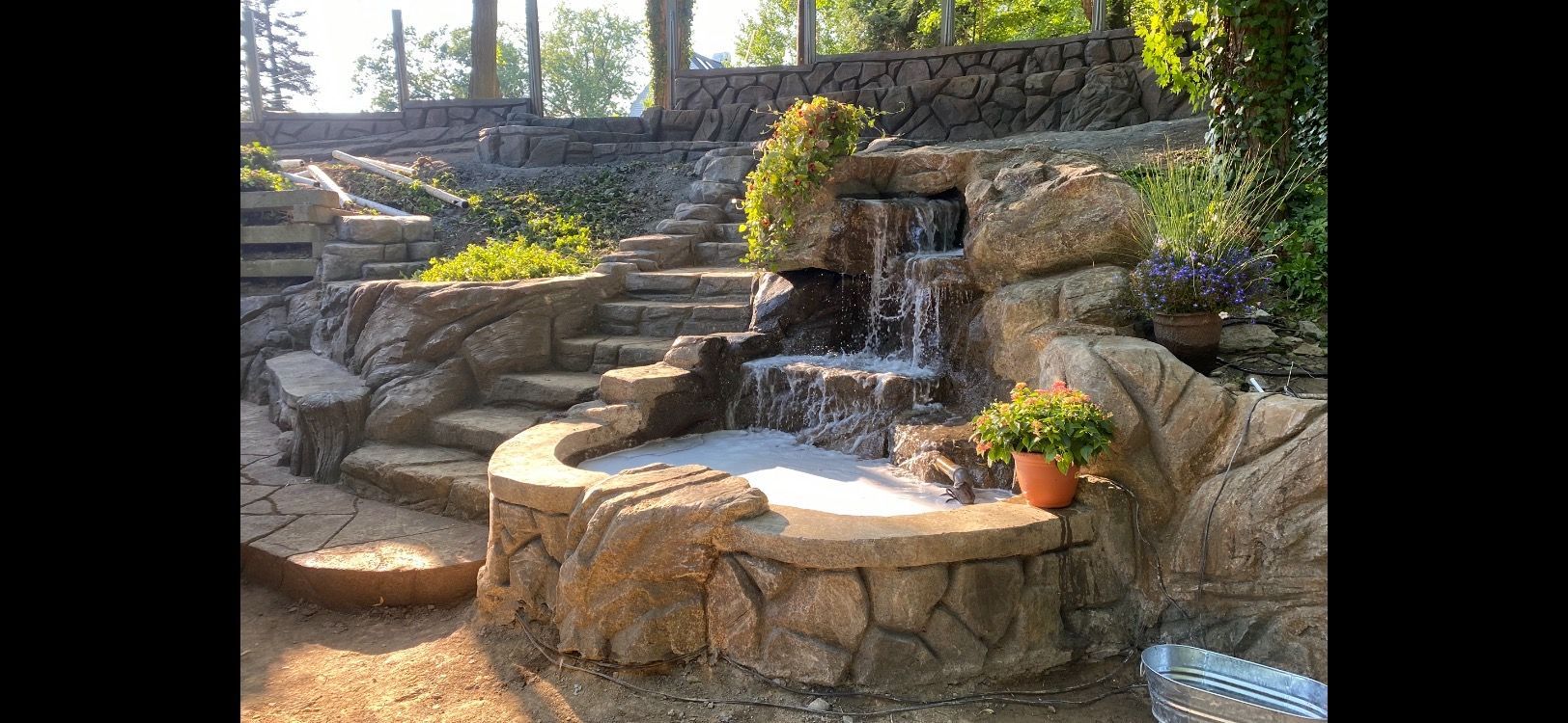 Luxury backyard waterfall with steps and potted plants, installed in Norman, OK by Elite Outdoor Living Solutions.