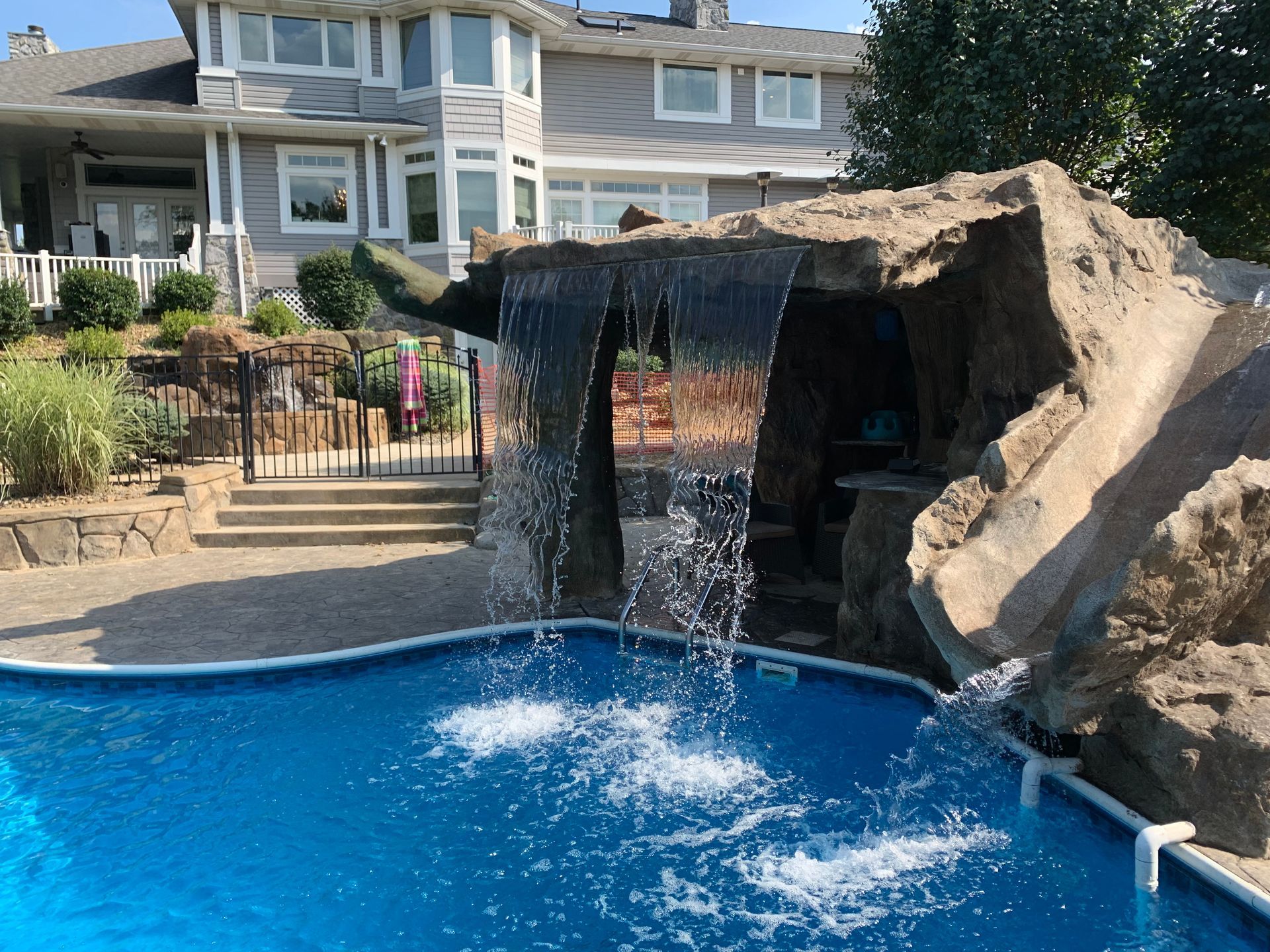 A large swimming pool with a waterfall and a house in the background