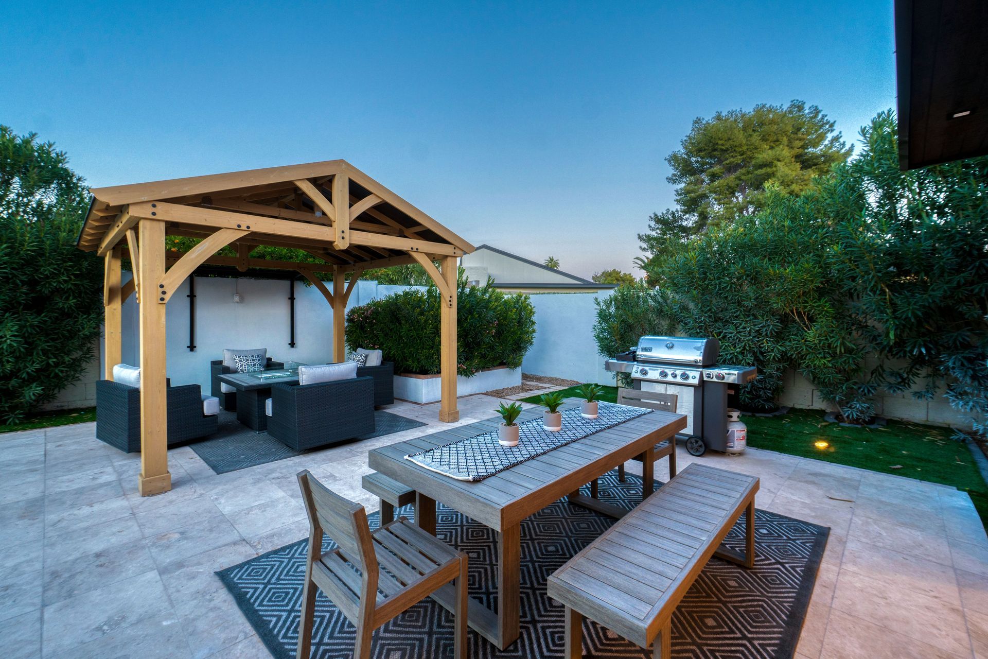 There is a table and benches under a gazebo in the backyard.
