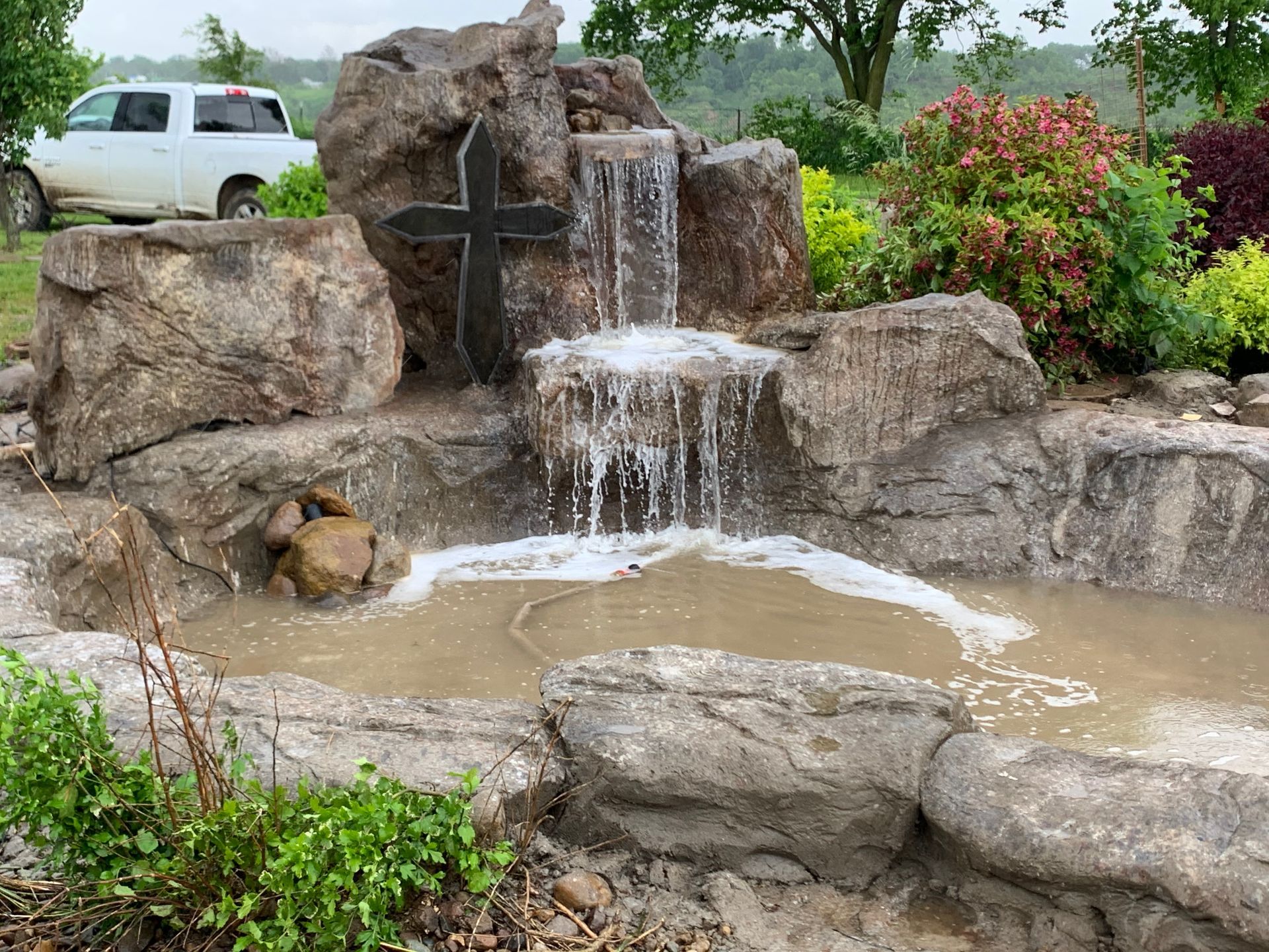 A waterfall in a garden with a cross in the middle of it.
