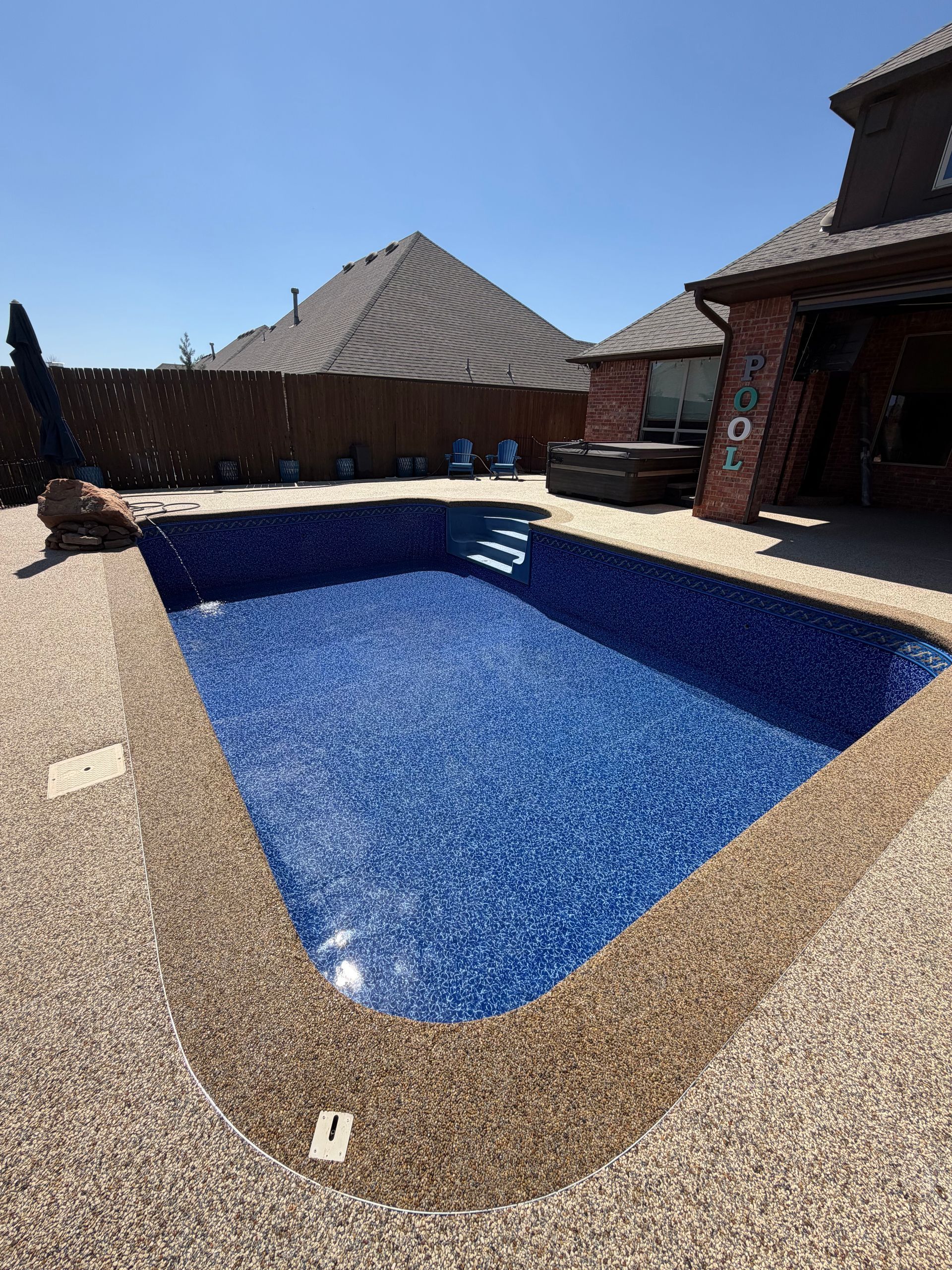 An empty, rectangular swimming pool with deep blue mosaic tiles and built-in steps next to a brick house patio.