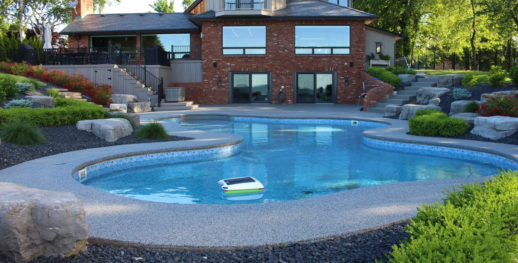 A rectangular hot tub with blue water sits on a dark wooden deck in a garden, surrounded by outdoor patio chairs.