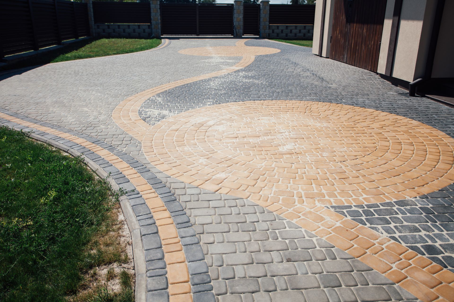 Curved brick and stone walkway with tan circular inlay beside grass and buildings