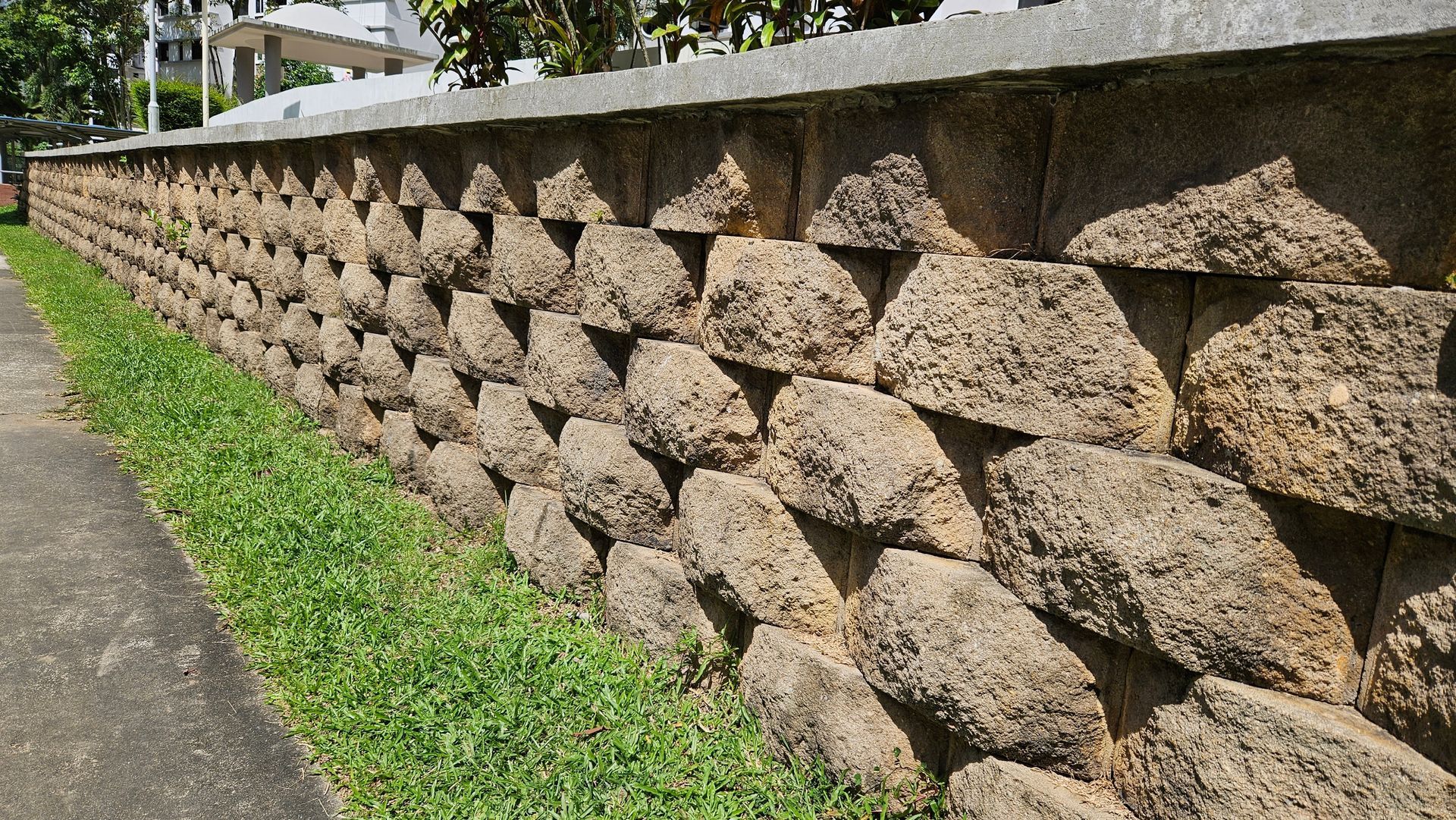 Stone retaining wall with stacked textured blocks beside a sidewalk and grass strip