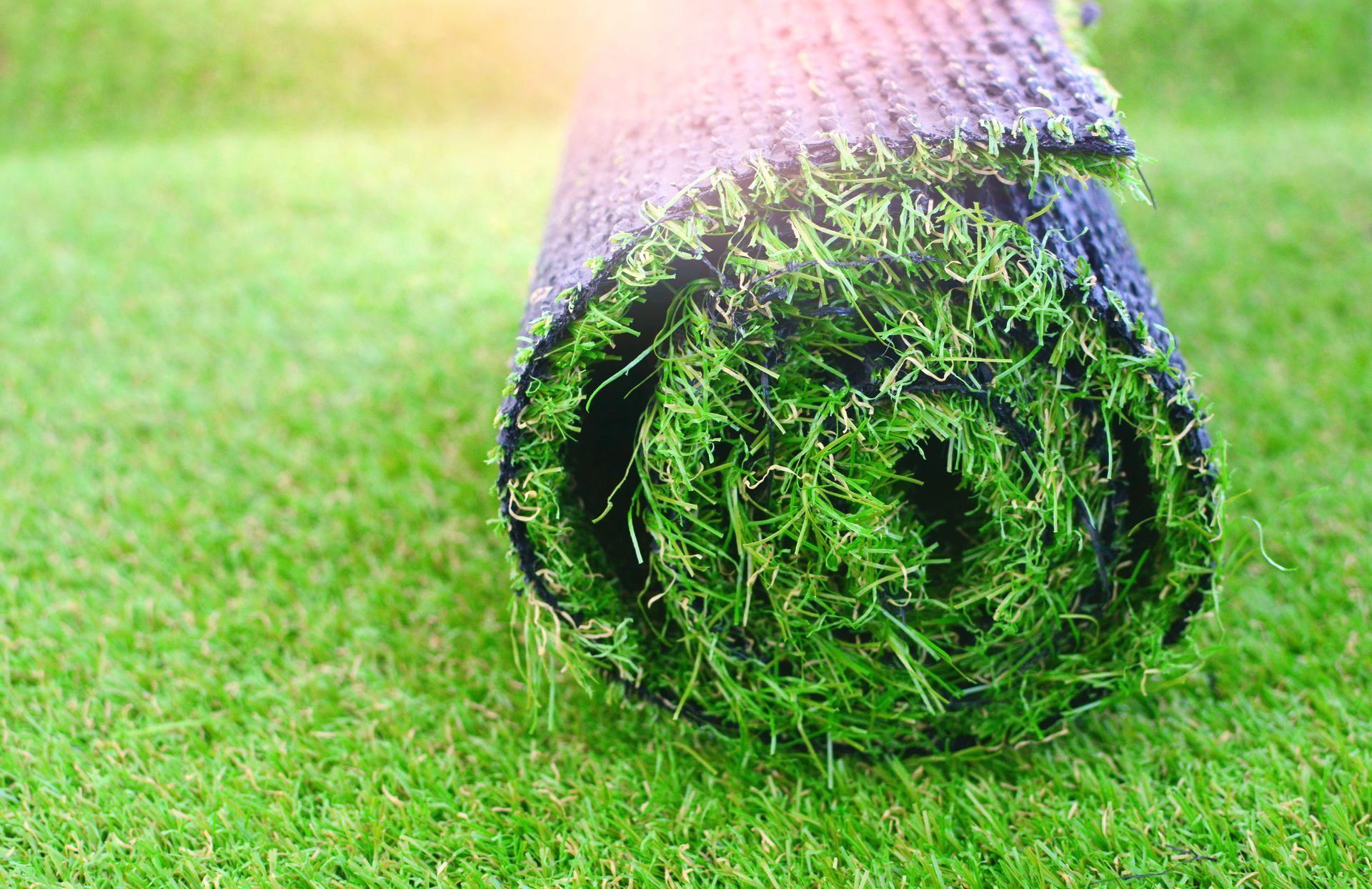 Close-up of a rolled artificial turf mat on green synthetic grass, showing detailed texture and backing material.