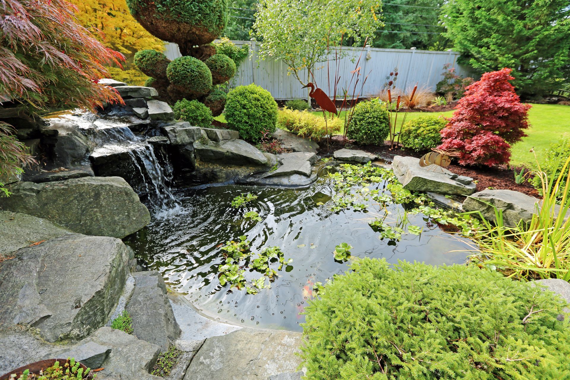 Rock-lined artificial waterfall flowing into a reflecting pond, installed by Elite Outdoor Living Solutions in Choctaw, OK.