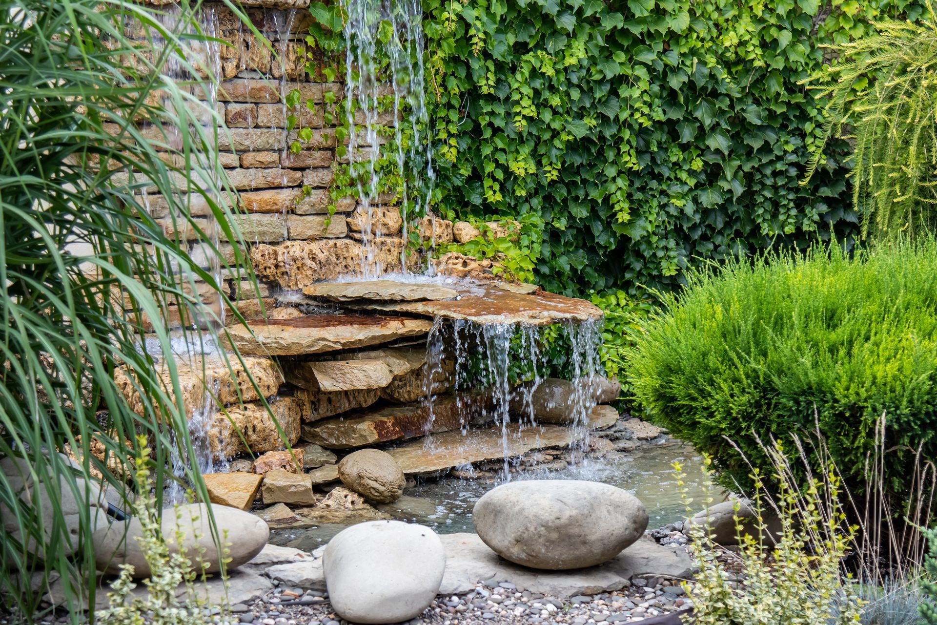 Brick and rock cascading waterfall surrounded by tall grass, installed in Edmond, OK by Elite Outdoor Living Solutions.