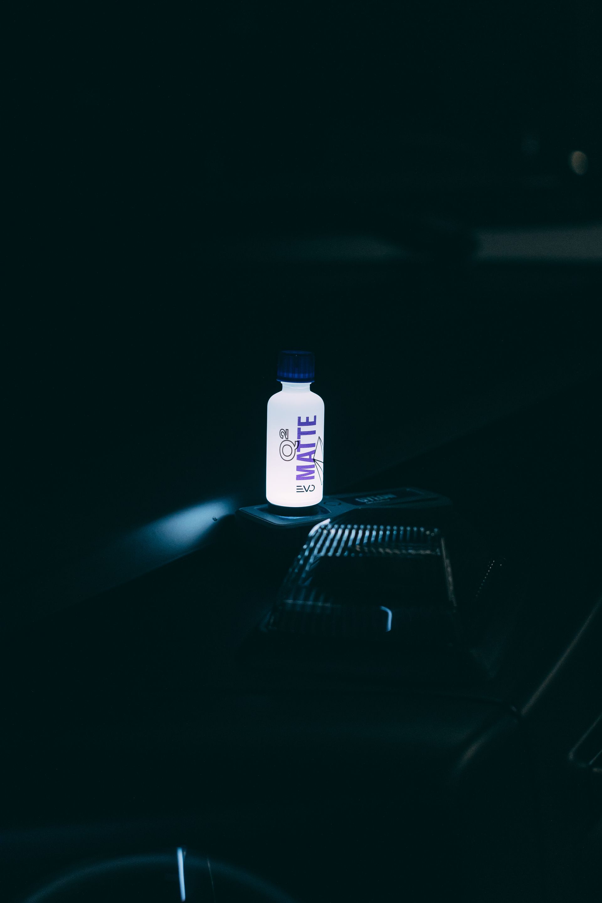White Bottle with Purple Label Standing on A Dark Car Hood — Straightline Detailing Cairns in Bungalow, QLD